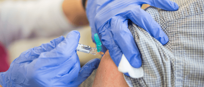 mãos com luvas azuis aplicando vacina no braço de uma pessoa. Campanha de vacinação contra a gripe