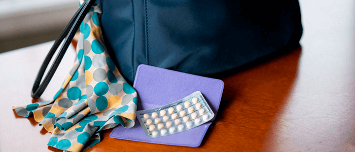 Cartela de anticoncepcional ao lado de bolsa feminina